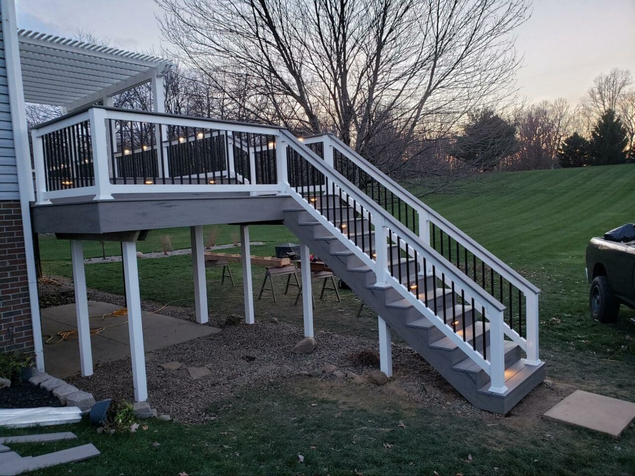 Photo of step lights and string lights that adorn an elevated deck with stairs and deck railing and pergola